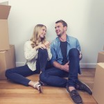 Young couple sitting in new house with packing boxes. They look like they have just moved in and they are very happy, smiling and talking. They sitting on the floor in casual clothes